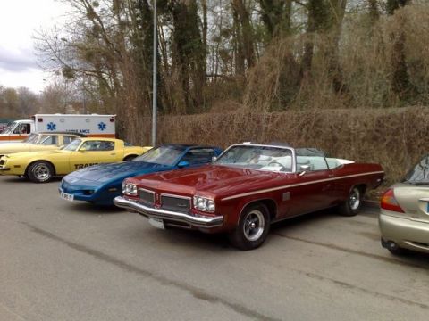 1991 Ford Crown Victoria - Several vintage vehicles are parked in a row, including a maroon convertible and a yellow sports car.