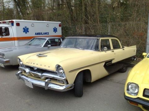 1991 Ford Crown Victoria - A vintage yellow and black Plymouth sedan is parked alongside an ambulance and another car.