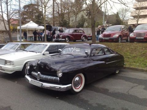 1991 Ford Crown Victoria - A dark coupe with a distinctive chrome grille and whitewall tires is parked at an outdoor event alongside other vehicles.