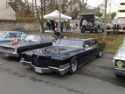 1991 Ford Crown Victoria - Several vintage cars are parked in a lot, with people gathered around tents in the background.