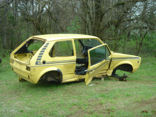 Stripped yellow Volkswagen Rabbit hatchback shell in a field