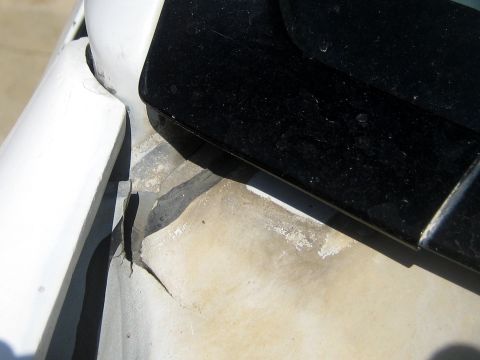 1996 Ford Bronco - Tight shot of damaged white bodywork where a black trim panel or removable top meets the body, showing torn and lifted paint with dull prim…