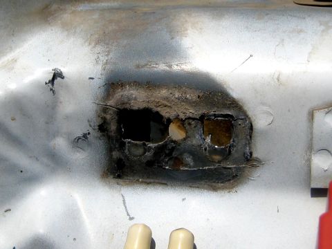 1996 Ford Bronco - Close-up of a rusted-out patch in white-painted sheet metal, likely a body mount or bracket location, where the metal has rotted through in…