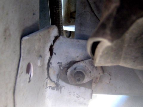 1996 Ford Bronco - Underside close-up of a white-painted bracket and body-mount stud with a nut and washer, showing rust seeping from a cracked seam in the me…