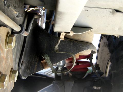 1996 Ford Bronco - Underbody view of a black rubber bump stop and mounting bracket bolted to the frame with yellow-zinc hardware, with a woven limit strap loo…