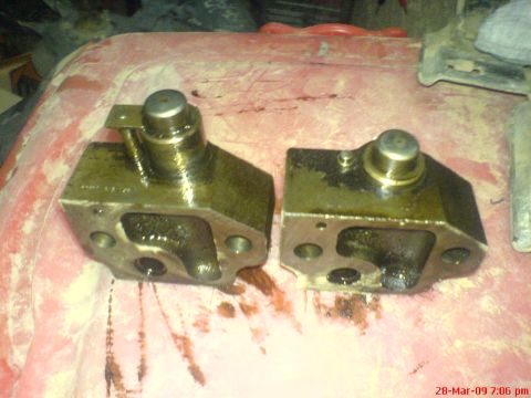 1992 Ford Crown Victoria - Two timing chain tensioners, likely from a Ford vehicle, are shown on a workbench.