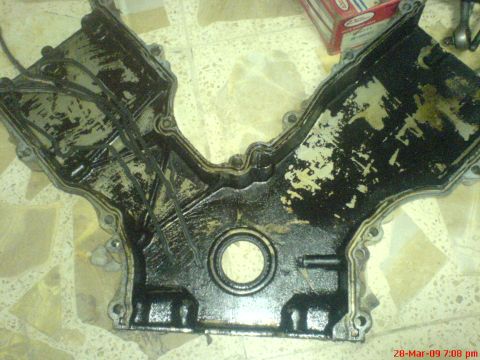 1992 Ford Crown Victoria - A V-shaped engine timing cover, covered in oil and grime, lies on a tiled surface.
