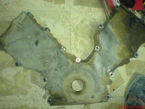 1992 Ford Crown Victoria - A dirty engine timing cover is shown lying on a tiled floor.