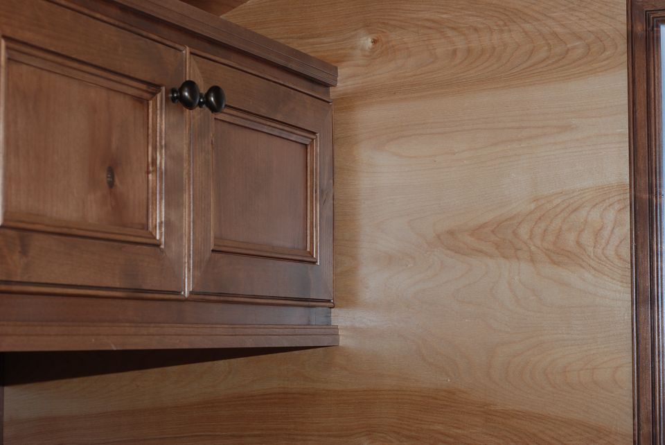 Wooden cabinets with dark knobs above a wood-paneled wall. A watermark is visible at the bottom right