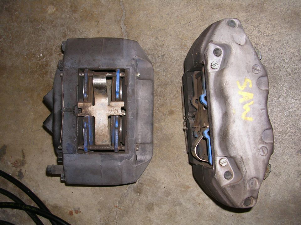 Two brake calipers, one dark gray and one silver with yellow writing that says 'SAW'