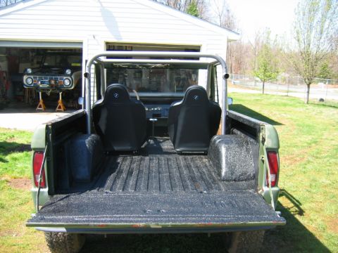 1992 Ford Mustang - Rear view through the dropped tailgate of a topless early Ford Bronco on grass, showing a spray-in bedliner coating the cargo floor, wheel…