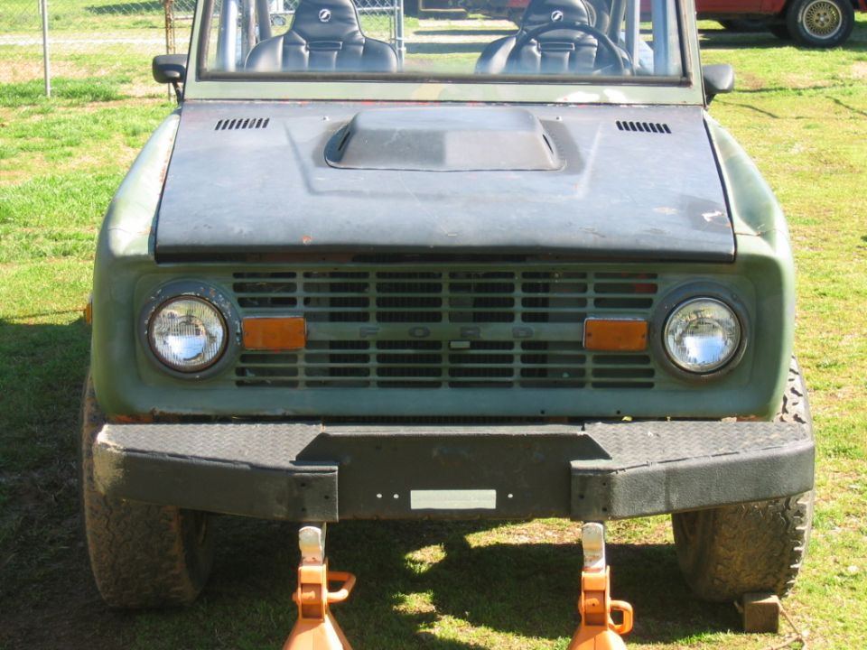 Green Ford Bronco front end on jack stands, with a hood scoop and diamond plate bumper