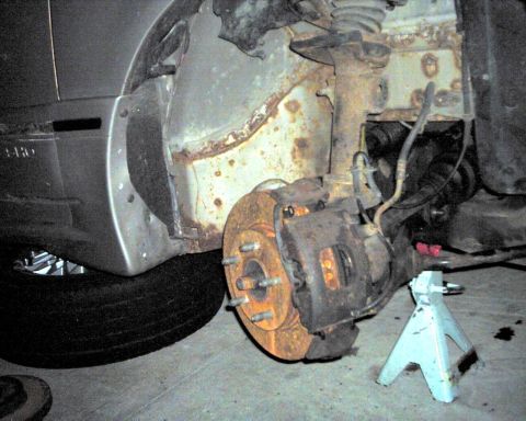 1990 Ford Taurus - The front wheel assembly of a car is shown, with significant rust on the brake components and suspension.