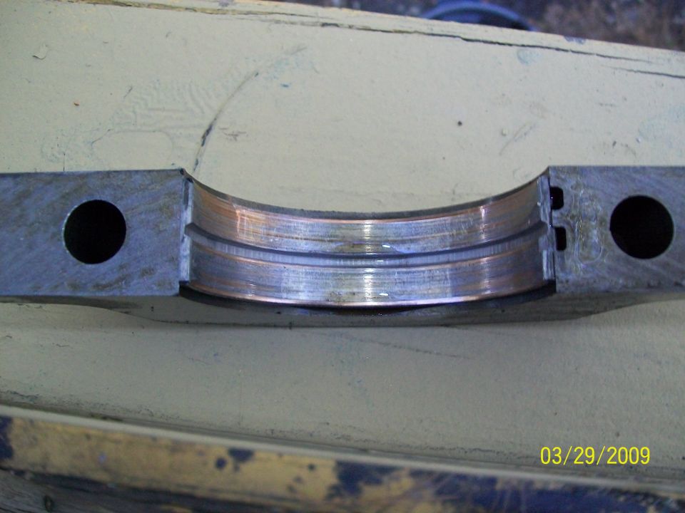 Engine bearing with copper-colored lining and metal housing, showing wear marks