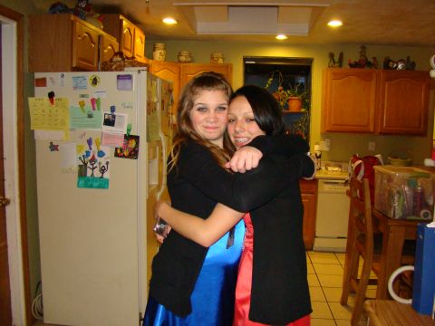 1989 Ford Bronco - Two young women embrace in a kitchen, with a refrigerator adorned with various papers and drawings.