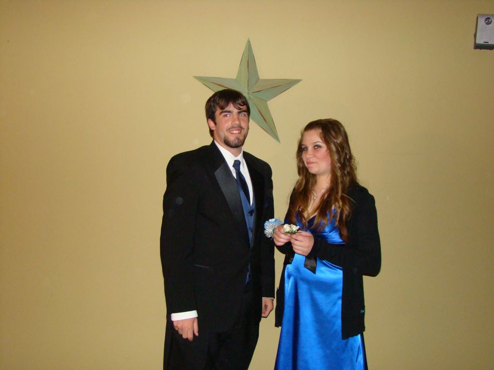 Couple in formal attire posing in front of a tan wall with a green star decoration