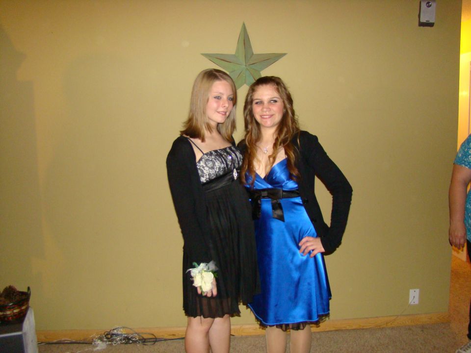 Two young women in formal dresses stand in front of a wall with a star decoration