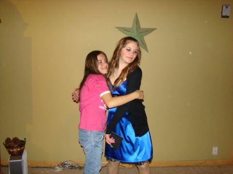1989 Ford Bronco - Two young women embrace in front of a decorated wall, one in a pink shirt and jeans, the other in a blue dress.