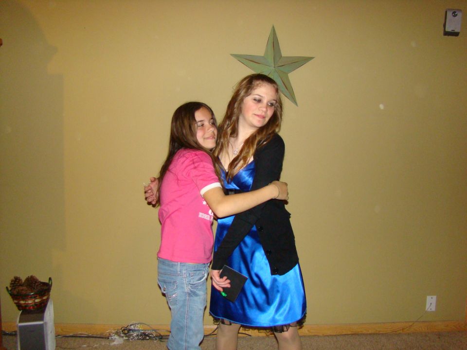 Two young women hugging in front of a yellow wall with a star decoration