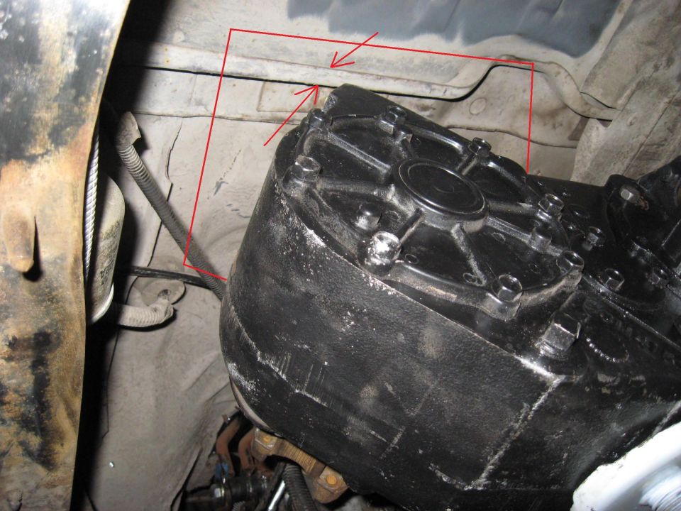 Close-up of a black transfer case with red arrows pointing to the frame above it