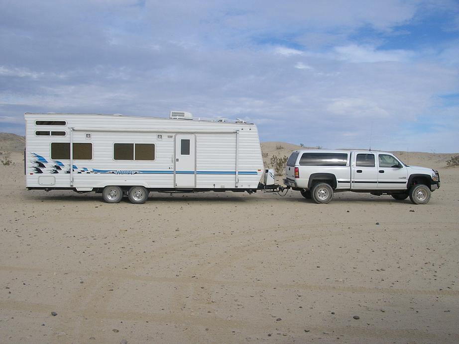 White Chevy crew-cab pickup towing a white toy hauler trailer in the desert
