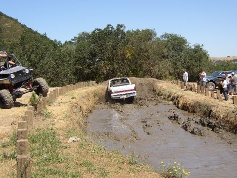 1989 Ford Bronco - Off-road vehicles tackle a challenging mud course on a sunny day.