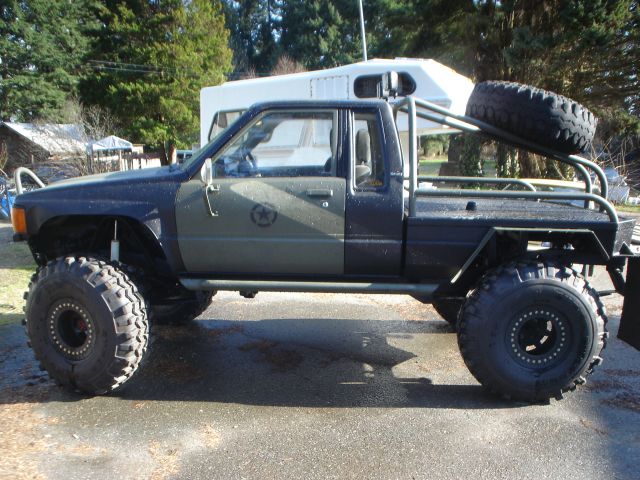 Modified pickup truck with large off-road tires and a spare tire mounted on a roll cage