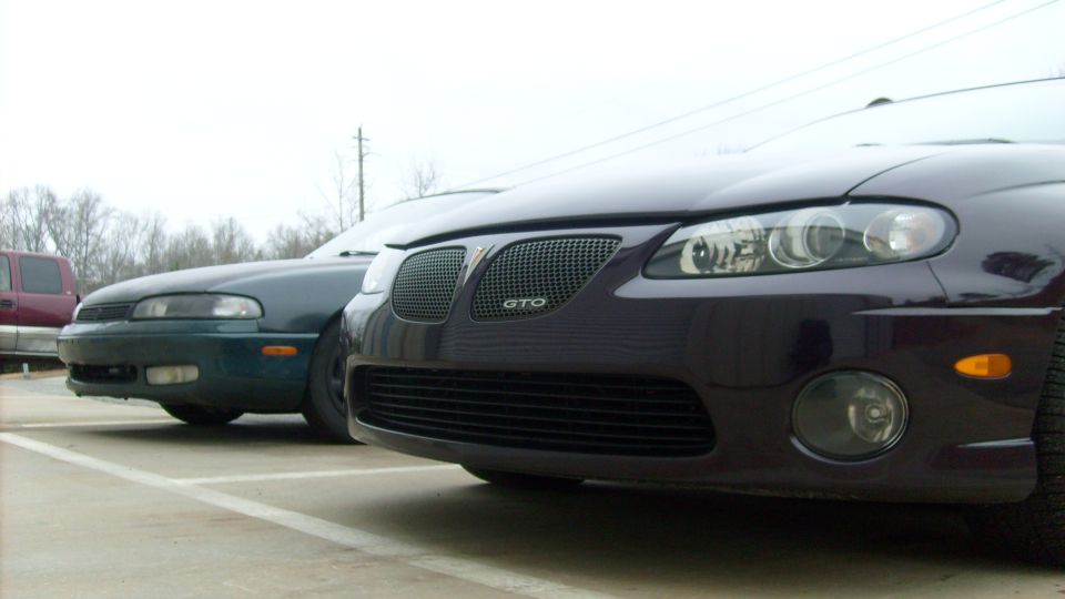 Front of a Pontiac GTO beside a sedan in a parking lot
