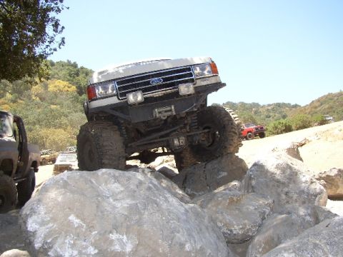 1989 Ford Bronco - A lifted Ford Bronco navigates a rocky off-road course with other vehicles in the background.