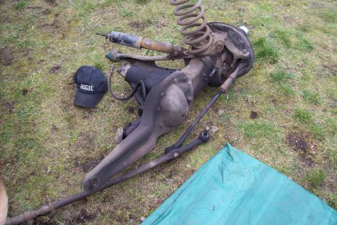 1995 Ford Bronco - Front axle assembly, shock, and coil spring laid out on grass next to a black hat with white text.