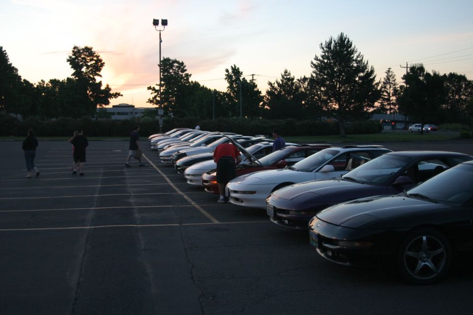 Row of sport coupes parked at a sunset car meet with people walking between them