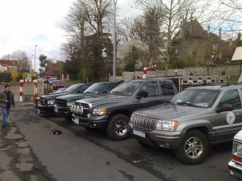 1991 Ford Crown Victoria - Several trucks and an SUV are parked in a line on a street, with a person walking nearby.