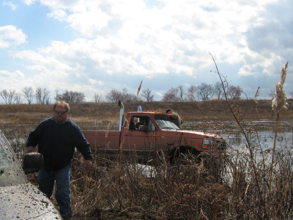 Orange pickup truck stuck in muddy water with a man walking nearby