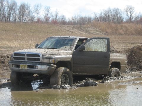 1990 Ford Bronco - A pickup truck is stuck in a muddy off-road area with its door open.