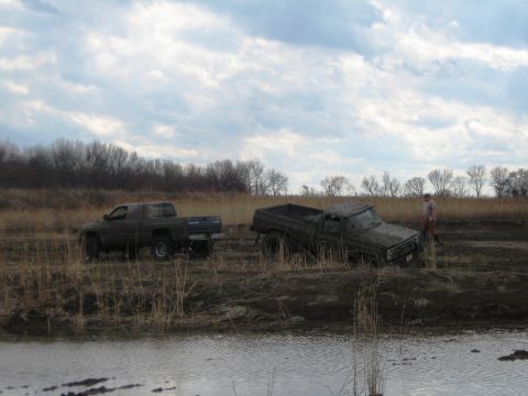 1990 Ford Bronco - Two trucks are stuck in a muddy field with a person standing near one of them.