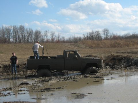 1990 Ford Bronco - A pickup truck is stuck deep in the mud with two people standing around it.