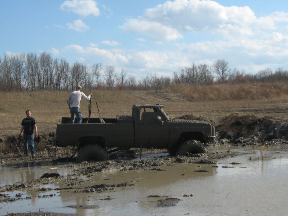 muddy pickup truck stuck in a mud pit with two guys nearby