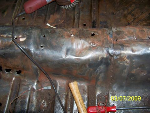 1974 Dodge Challenger - The interior floor pan of a vehicle shows significant rust and damage, with tools present for repair.