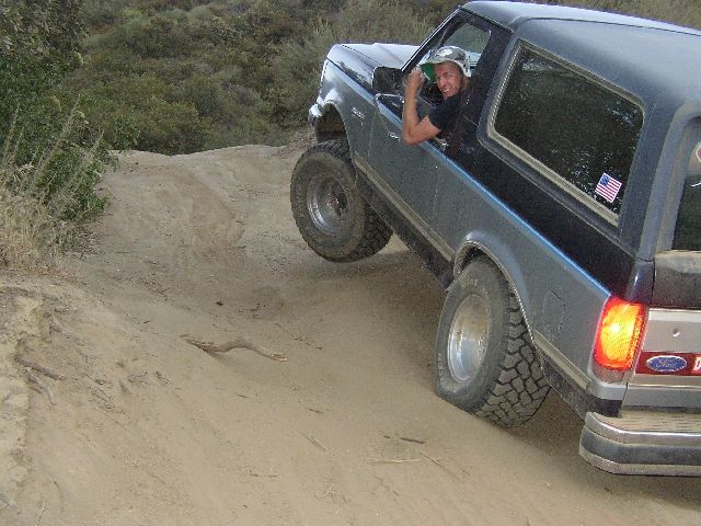 Blue Ford Bronco on sandy off-road trail with driver waving from window