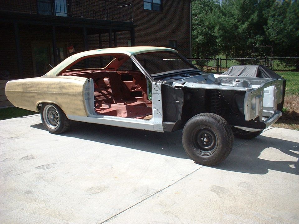 Stripped 1967 Mercury Cyclone coupe in primer, side view, missing doors, fenders and hood on concrete driveway