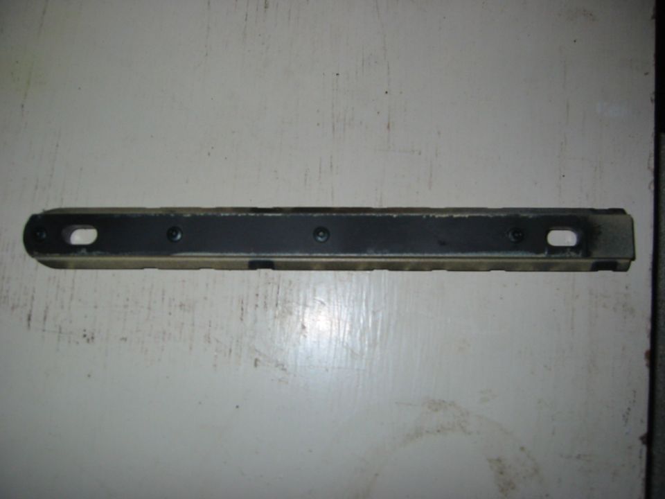 Metal bracket with two oval holes and three screw holes, lying on a white surface