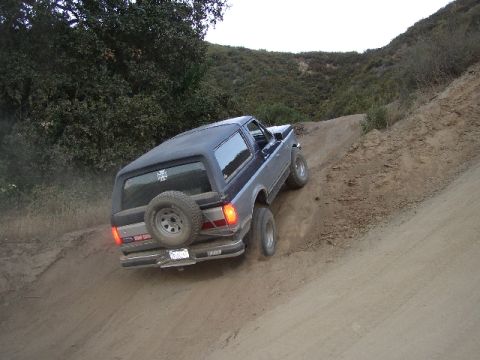 1989 Ford Bronco - A Ford Bronco navigates a steep dirt incline, its rear visible as it climbs.
