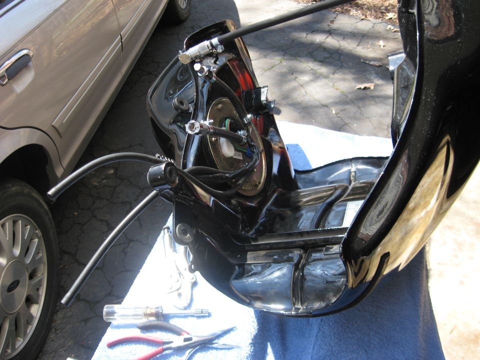 Disassembled black motorcycle headlight fairing with wiring, on cloth with tools