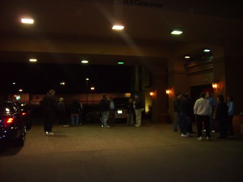 1993 Ford Crown Victoria - People stand under a covered area at night, with vehicles parked nearby.