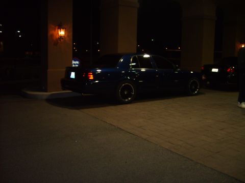 1993 Ford Crown Victoria - A dark blue sedan is parked outside a building at night, with another vehicle visible in the background.