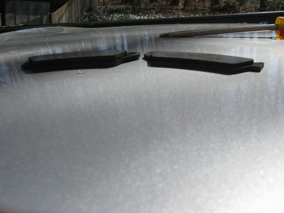 Two worn brake pads and a screwdriver lying on a silver panel outdoors