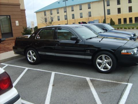 1993 Ford Crown Victoria - A black sedan is parked in a lot next to a blue car and a white car.