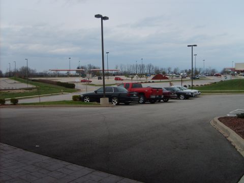 1993 Ford Crown Victoria - A black 1993 Ford Crown Victoria is parked in a lot with other vehicles under an overcast sky.