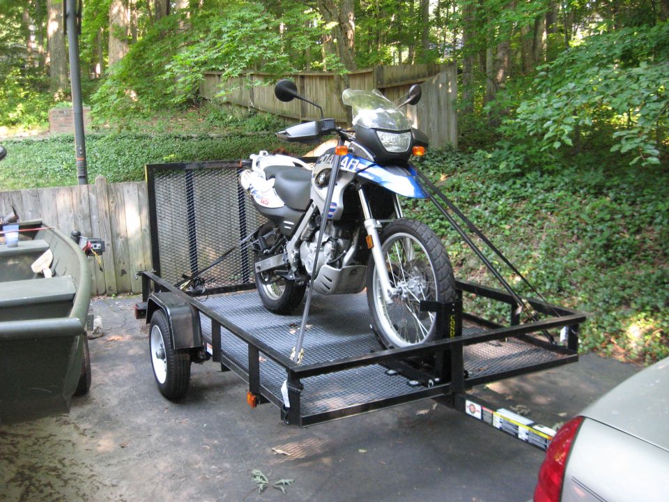 White and blue BMW dual-sport motorcycle strapped on a black utility trailer outdoors