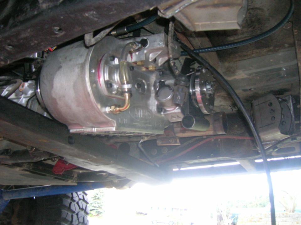 Underside view of a vehicle's transmission and transfer case assembly with metal lines and hoses attached